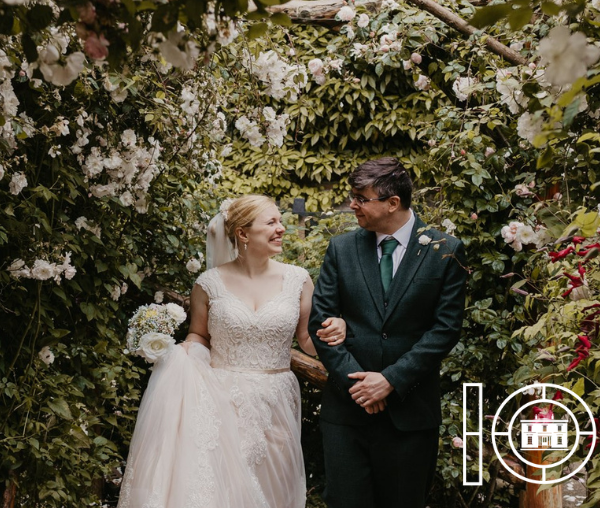 Bride and groom walk under pergola in garden