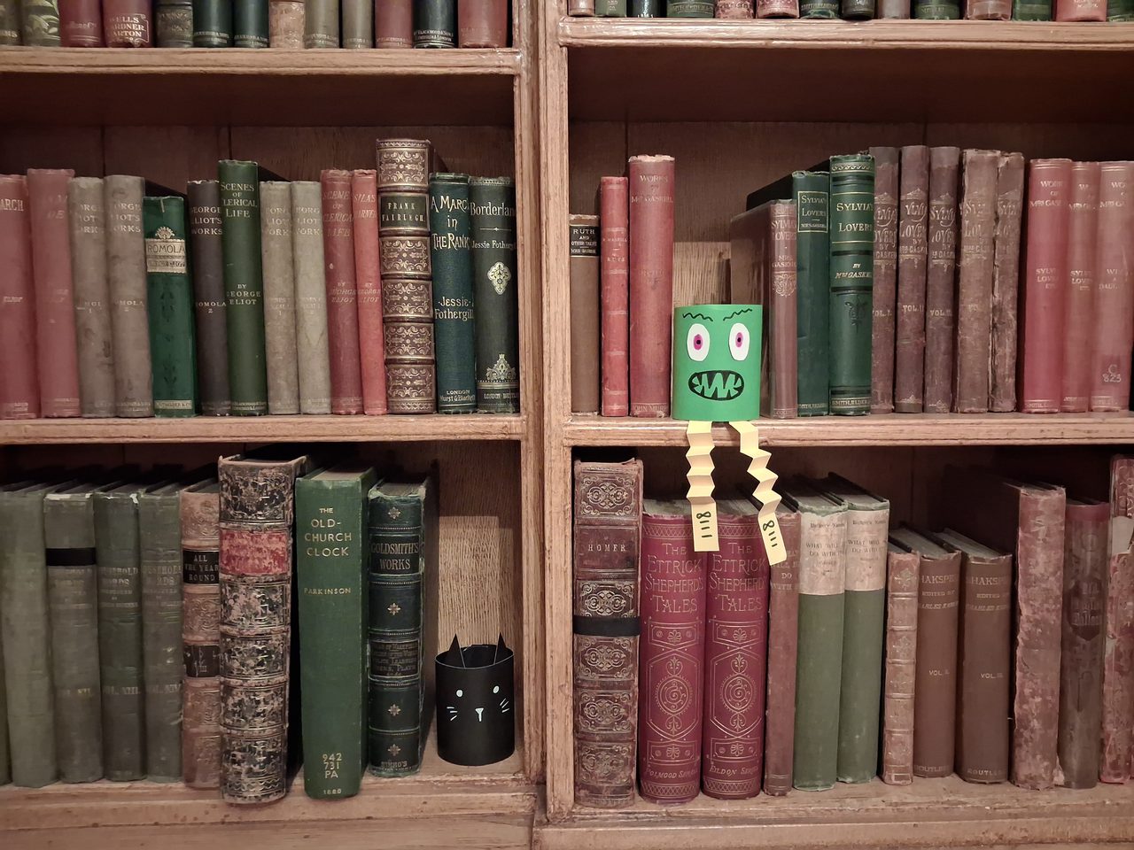 A hand crafted monster and cat sat on a shelf of old books. 