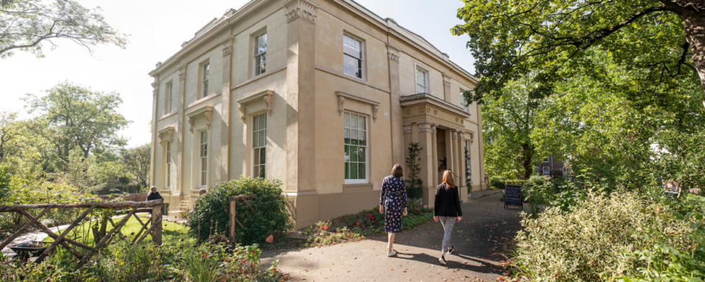 A large Victorian house with two visitors walking up the garden path