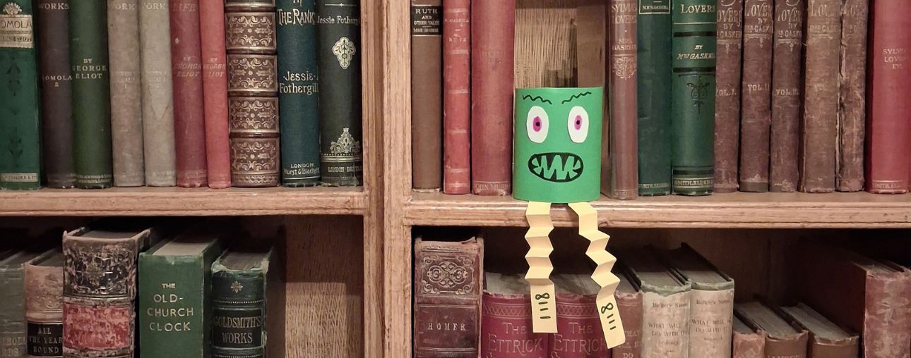 A hand crafted monster on a shelf of old books